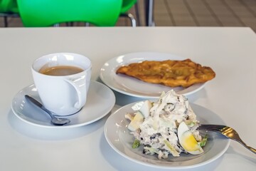 A cup of coffee, a plate of salad with eggs, and a pastry are arranged on a white table, with vibrant green chairs in the background