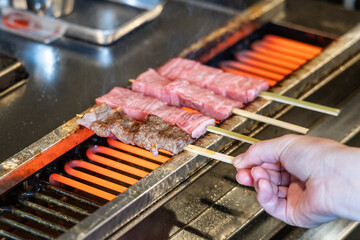 Hand barbecuing the delicious hida beef with high marbling on skewers at street market in Takayama