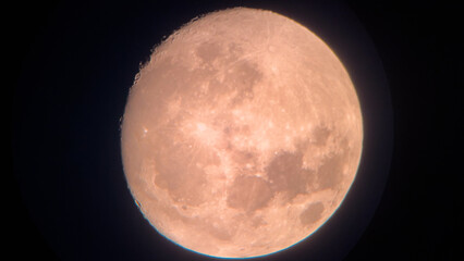 Full moon shining brightly in the dark night sky. Stunning close-up view of the full moon with a warm orange hue, detailed surface texture visible. Night sky astronomy background.