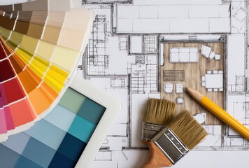 Top-down view of a floor plan with paint swatches, brushes, a pencil, and a tablet suggesting interior design or renovation planning