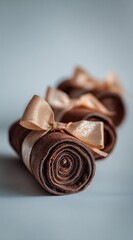 Three brown suede rolls, tied with light gold ribbons, are arranged diagonally with a bright background, exhibiting minimalist elegance
