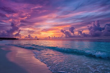 Tropical sunset over a tranquil beach.  Soft, colorful clouds paint the sky as the sun dips below the horizon, casting a vibrant hue on the ocean and shore
