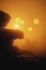 Golden sunrise over misty cliffs.  Silhouette shapes of craggy terrain.  Soft, glowing light