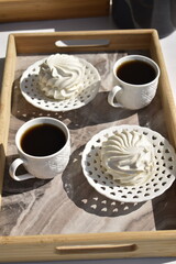 two cup of black coffee and two marshmallows on decorative white plates on marble surface tray
