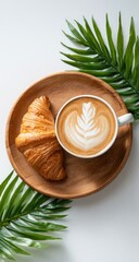 Latte and croissant on a wooden plate with palm leaves