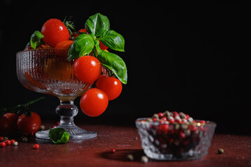 Red cherry tomatoes and basil arranged in glass bowl on dark table for clean eating and vegan lifestyle themes