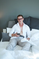 A portrait of a sexy young businessman in a white shirt, looking at his cell phone while relaxing on the sofa at home.