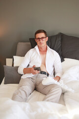 A portrait of a sexy young businessman in a white shirt, looking at his cell phone while relaxing on the sofa at home.