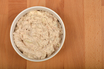 A bowl of homemade tuna and cream cheese spread is placed on a wooden board with ample copy space