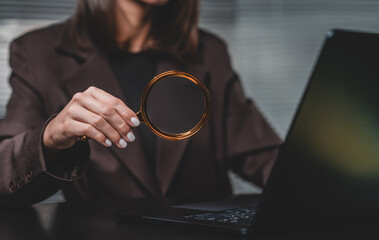 Woman holding magnifying glass in front of laptop screen in offi