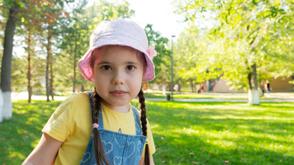A 4-year-old girl in a pink panama hat against the backdrop of a summer park. High quality photo
