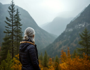 A back view of a woman with gray hair, gazing at a serene, misty mountain landscape with vibrant autumn foliage. Themes: contemplation, adventure, and nature.