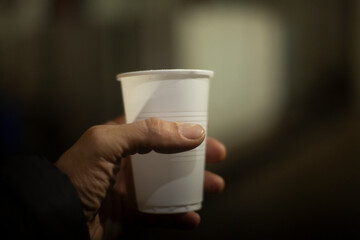 Glass of water. Plastic dishes. A hand holds a white glass of water.