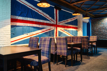 A cozy and stylish restaurant or English-style pub interior with checkered chairs, brick walls, and the Union Jack flag of Great Britain. United Kingdom. UK decor