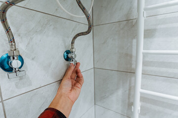 In a chic bathroom, a skilled professional adjusts a water valve. The stylish tiles and elegant heated towel rack showcase modern design, blending functionality with luxury