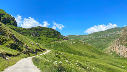 The mountain road winds through a lush green valley with blue skies and white clouds overhead. A trip to Azerbaijan © chekart