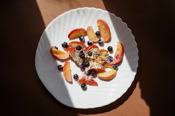 Fruit yogurt with peaches, blueberries and granola on brown background