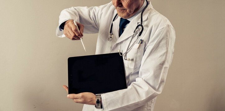 Doctor in white coat with stethoscope pointing at digital tablet using stylus, senior physician showing healthcare technology for online consultation, telemedicine and medical innovation