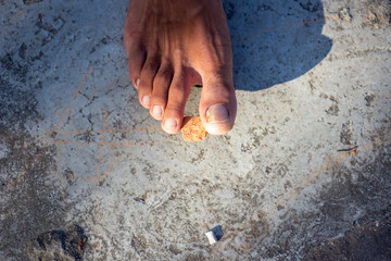 Closeup of a persons foot stepping on a small crumb on a textured surface
