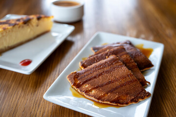 A plate of pancakes with syrup on top is on a wooden table. The pancakes are stacked on top of each other