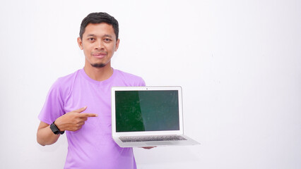 Happy asian man wearing purple t-shirt and holding laptop computer working online and looking at camera isolated on white background, online education