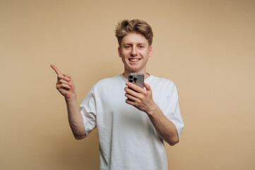 portrait of young man points energetically while holding his smartphone, illustrating a sense of...