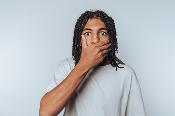 portrait of surprised young man covering his mouth, convey shock and disbelief on white background