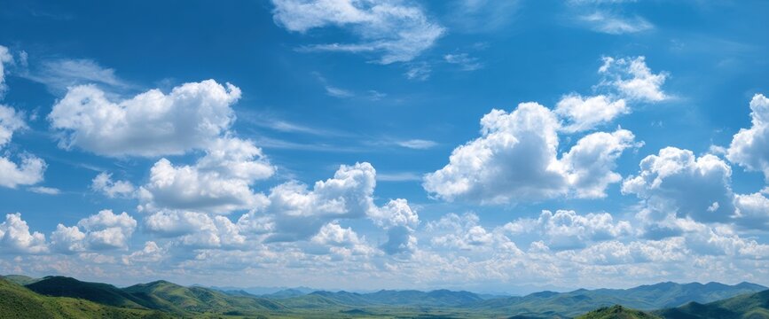 Expansive sky filled with fluffy white clouds over rolling green hills
