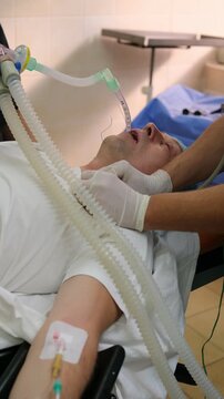 Medical professionals carefully managing patient airway through precise intubation, using specialized equipment in sterile hospital setting while ensuring optimal respiratory support. Vertical video