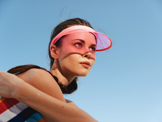A young athletic woman wearing a pink visor leans forward in an energetic action pose, set against a vivid blue sky and bright daylight.