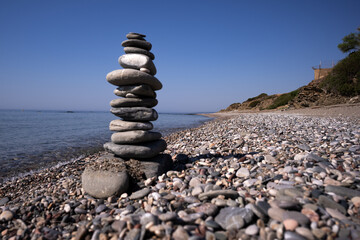 a stonework of flat pebbles keeps an even balance on the sea beach under the blue sky