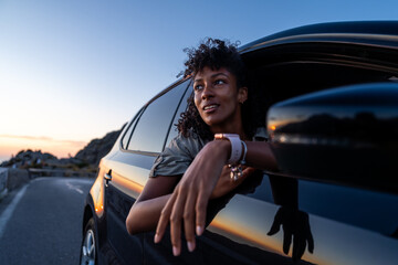 Young woman enjoys golden hour scenery from car window. Concept of freedom, sunset drive, peaceful...