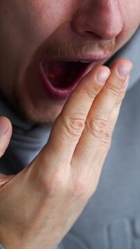A man covers his mouth with his hand when he yawns.
A tired man yawns in a room.
A man opens his mouth wide when he yawns and covers it with his palm.
A sleepy and tired man