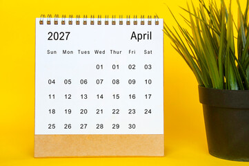 April 2027 monthly desk calendar design with clean white layout, yellow background, and green plant...
