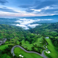 Foto auf Acrylglas Grün Aerial view of lush golf course landscape at sunrise, surrounded by rolling green hills and misty clouds, creating serene atmosphere  © Dounonji