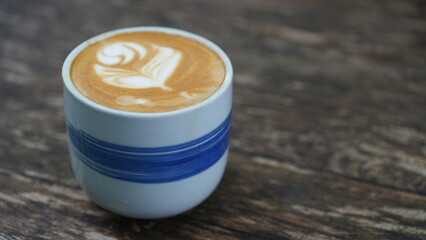 Cup of hot cappuccino with latte art on wooden table. Image in top view.