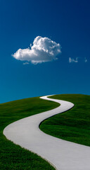 Naklejka premium A winding white path leads through a lush green hill under a vast blue sky with a single cloud