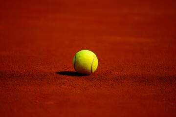 A bright yellow tennis ball sits on the red clay court, ready for the next serve or volley