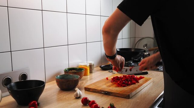 In a tidy kitchen, a person finely chops fresh tomatoes and garlic on a wooden cutting board as they prepare ingredients for a meal. Bright, inviting atmosphere enhances cooking experience