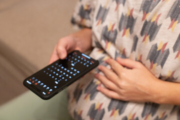 Pregnant woman gently touching her belly and looking at calendar in her phone. Baby birth date...