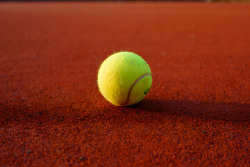 Closeup of a tennis ball on a red clay court, capturing the texture and vibrant color of the ball