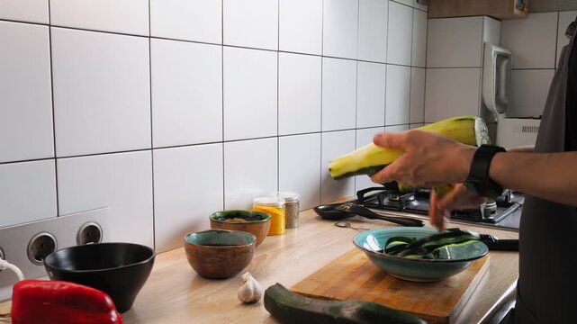 A person skillfully chops zucchini and prepares fresh ingredients, including garlic and bell peppers, in a modern kitchen. Sunlight brightens the workspace