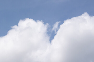 A wideangle view of a clear blue sky with a fluffy white cloud formation stretching across the bottom and a smaller cloud in the upper corner.The image is an ideal background symbolizing calmnes