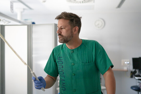 Surgeon wearing green scrubs holding medical equipment in hospital operating room