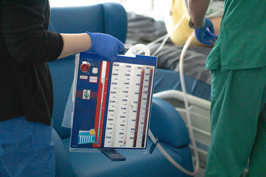 Nurse holding chest drainage system with patient in background in hospital room