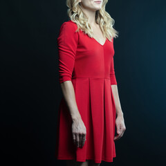 Fototapeta premium Elegant blonde woman posing in red dress on black background