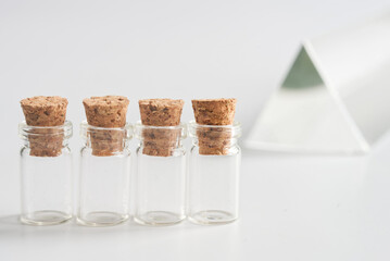 Four clear glass vials with cork stoppers in a row on white, a glass prism behind; clean lab still...