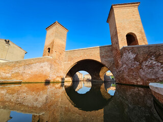Historic Trepponti bridge with twin towers reflecting in calm canal waters in Comacchio, Emilia-Romagna, Italy