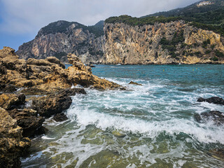 Rocky coastline with waves crashing and turquoise water below steep cliffs at Paleokastritsa, Corfu, Greece