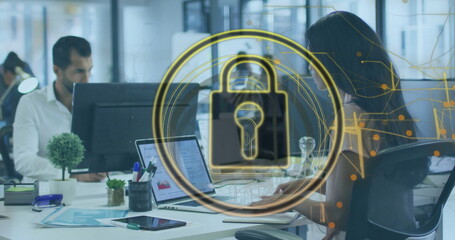 Typing Asian woman working on laptop at modern open-plan office desk, with monitor and plants